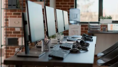 Fileira de monitores e teclados em mesa de escritório, equipamentos de TI e sua vida útil