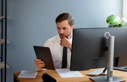 TCO locação de TI Profissional analisa tablet em frente a monitor, comparando custos de locação de TI e compra