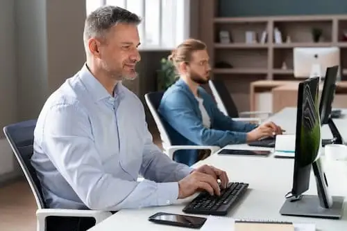TCO locação de TI Dois profissionais trabalhando em computadores de mesa em escritório corporativo, com locação de TI