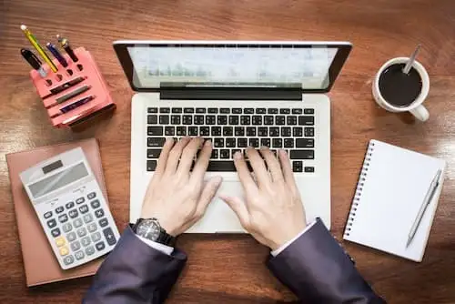 Locação de TI OPEX Mãos digitando em notebook ao lado de calculadora e café, gestão financeira de TI
