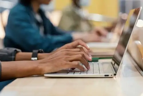 Mãos digitando em notebook locado em ambiente de trabalho compartilhado
